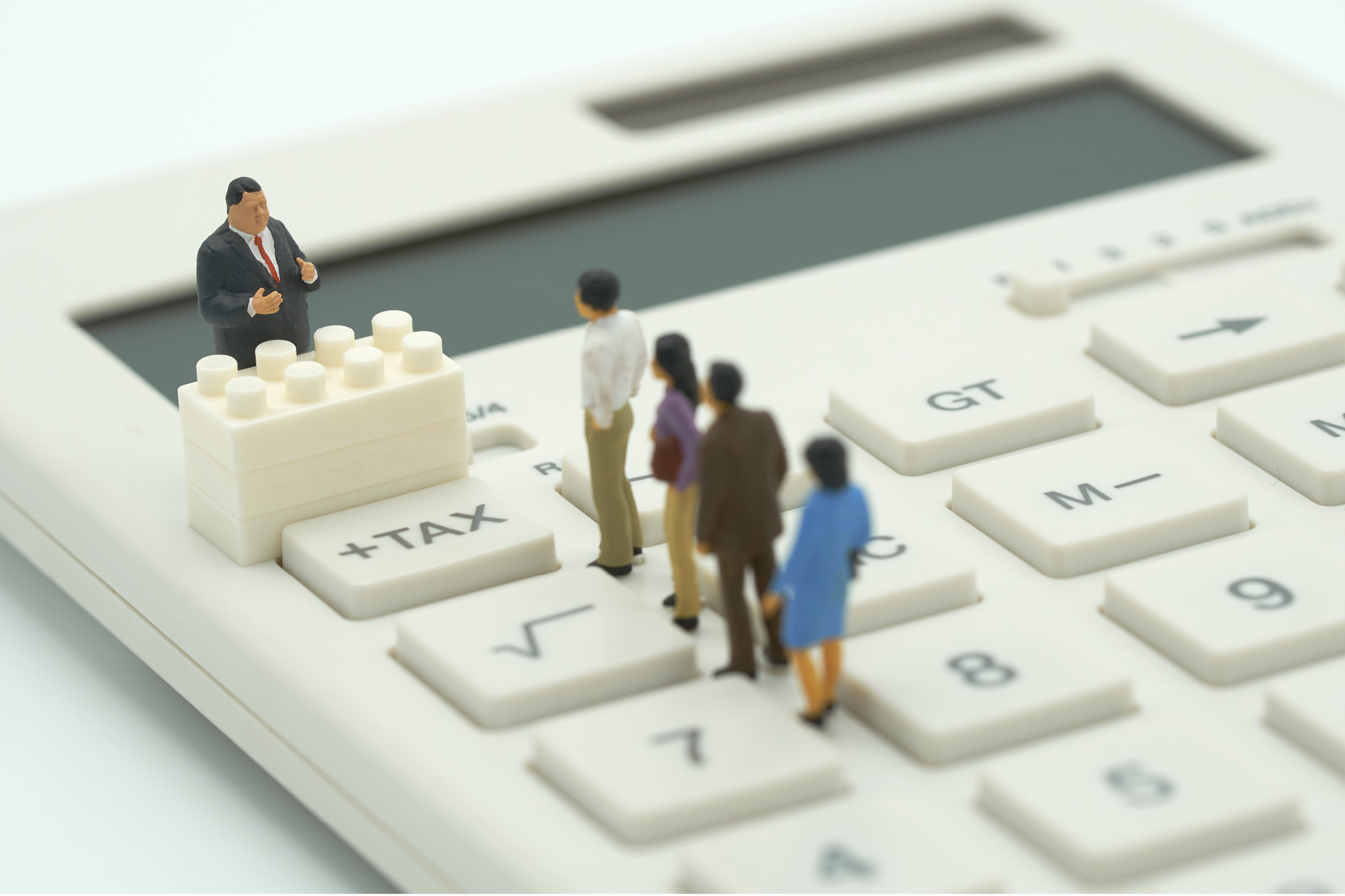 Four miniature people in a queue on a calculator. One miniature person stood next to a button that reads tax.